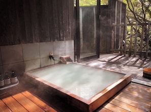 Un jacuzzi con cubierta de madera, pared de azulejos y valla de madera.