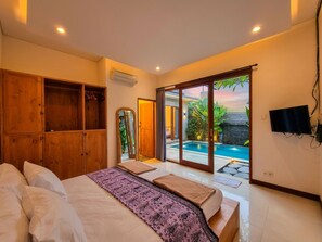 Ein Schlafzimmer mit Bett, Holzschrank und Blick auf einen Swimmingpool durch eine Glastür.