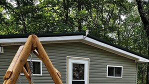A wooden swing set in front of a house with a black metal fence.