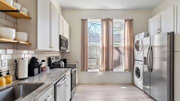 A modern kitchen with a stainless steel refrigerator, microwave, and oven, wooden cabinets, and a window with curtains.