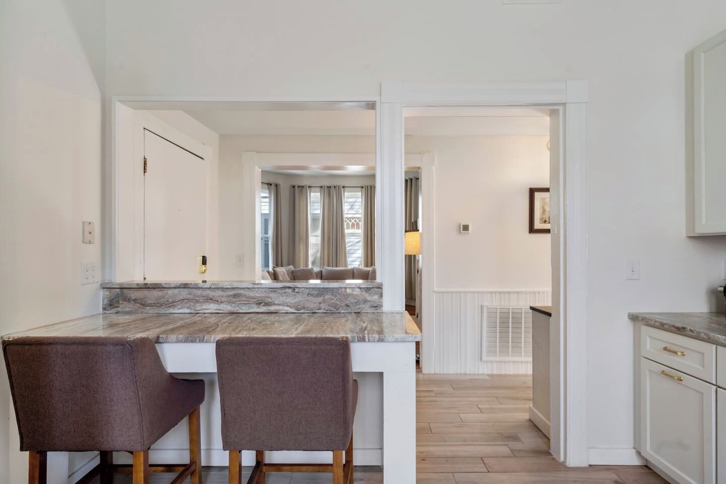 A modern kitchen with a marble countertop, two chairs, and a view into a dining area.