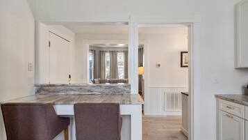A modern kitchen with a marble countertop, two chairs, and a view into a dining area.