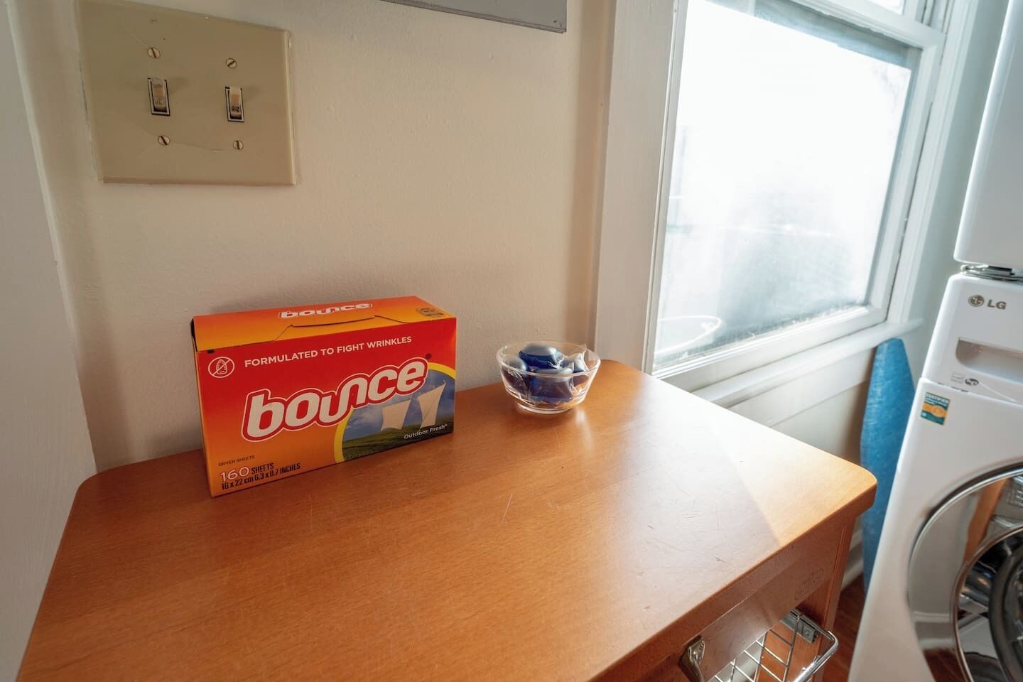 A box of Bounce dry shampoo on a wooden table next to a window.