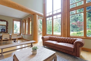 A spacious room with large windows, a fireplace, a dining area, and a comfortable seating area. - Cozy ski chalet on Nicklaus North Golf Course (Whistler)