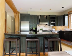 A kitchen with dark wooden cabinets, a stainless steel refrigerator, a central island with stools, and a window providing natural light.