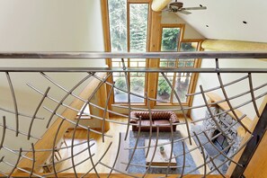 A high-ceilinged room with a wooden floor, a fireplace, and a view through a window to a balcony.