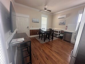 A kitchen with wooden flooring, a dining table with chairs, a refrigerator, and an air conditioning unit. - Cozy 2-bedroom house in pleasant Apalachicola with AC (Apalachicola)