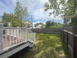 Ein Garten mit Holzterrasse, weißem Zaun und Rasenfläche.