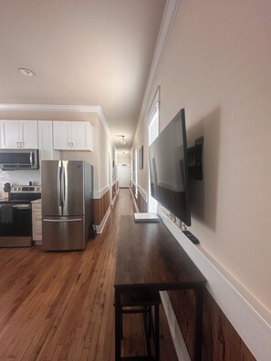 Een moderne keuken met roestvrijstalen apparatuur, een houten vloer en een flatscreen televisie aan de wand.