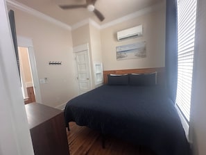A bedroom with a bed, a ceiling fan, an air conditioning unit, a door, and a painting on the wall. - Cozy 2-bedroom house in pleasant Apalachicola with AC (Apalachicola)