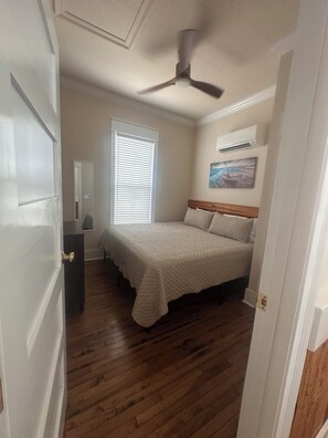 A bedroom with a bed, a ceiling fan, a window with blinds, a dresser, and an air conditioning unit. - Cozy 2-bedroom house in pleasant Apalachicola with AC (Apalachicola)