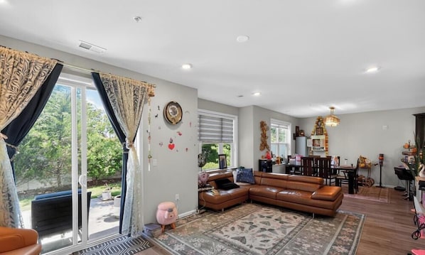 A spacious living room with a brown leather sofa, a patterned rug, and a dining area with a chandelier.