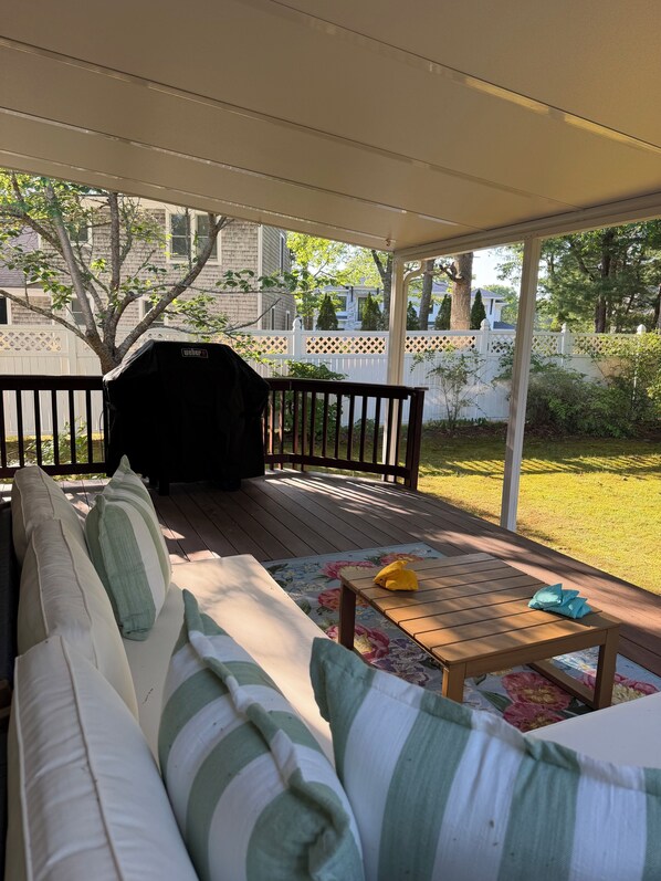 A covered outdoor seating area with a wooden deck, a white fence, and a view of a residential neighborhood. - Gorgeous 3-bedroom house close to Willowbend, New Seabury in charming Mashpee (Mashpee)
