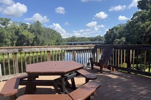 A wooden deck with picnic tables and chairs overlooking a lake. - Townhome in Temple Terrace |Community Pool & Dock on the Hillsborough River |Near USF & Busch Garden (Tampa)