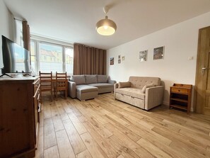 Ein Wohnzimmer mit einer Couch, einem Sessel, einem Fernseher, einem Holzschrank und einer Deckenleuchte.