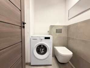 Une petite buanderie équipée d’un lave-linge et de toilettes.