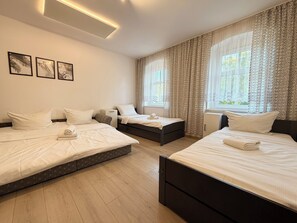 A hotel room with three beds, a small desk, and a window with patterned curtains.