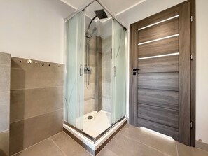 Une salle de bain moderne avec une douche à parois de verre, une porte en bois aux lignes horizontales et des murs carrelés.