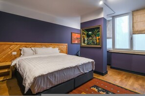 Ein Schlafzimmer mit einem Bett mit Holz-Kopfteil, einer lilafarbenen Akzentwand, einem gerahmten Gemälde und einem Fenster mit Jalousien.