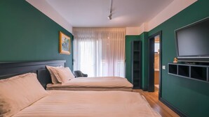 Quarto de hotel com duas camas, televisão e janela com cortinas translúcidas.
