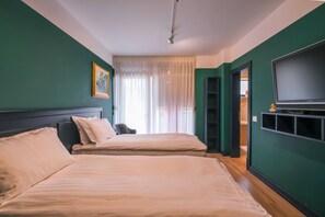 Ein Hotelzimmer mit zwei Betten, einem Fernseher und einem Fenster mit durchsichtigen Vorhängen.