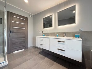 Une salle de bain moderne avec une douche à parois de verre, un meuble-lavabo double avec un grand miroir et une porte en bois foncé.