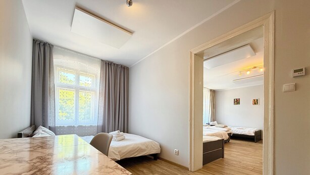 A modern hotel room with a marble table, two beds, a wooden floor, and a large window with curtains. - Park Leśnicki Homely Studio #3 (Wrocław)