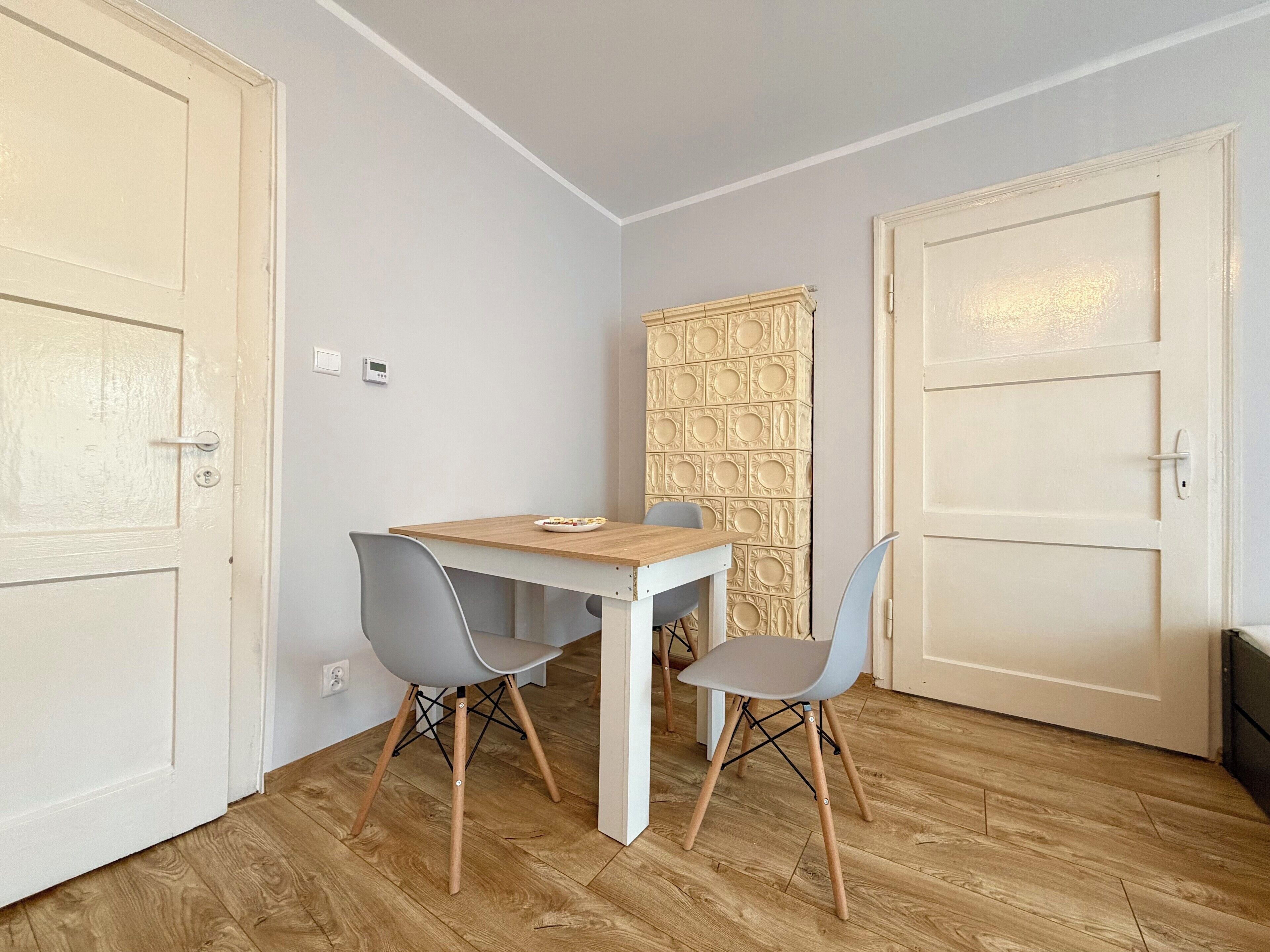 A small room with a wooden table, two chairs, a wall-mounted radiator, and a door.