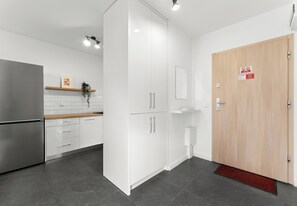 A modern kitchen with white cabinets, a stainless steel refrigerator, and a wooden door with a sign. - Górka Narodowa Chic Apartment (Kraków)