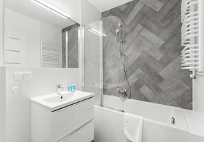 Un baño moderno con ducha de vidrio, lavamanos blanco y un perchero para toallas.