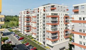 Un edificio residencial de varios pisos con balcones, un estacionamiento y un área verde al fondo.