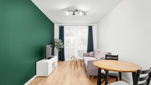 Uma sala de estar moderna com um sofá, uma mesa redonda de madeira, uma televisão e uma pequena mesinha de apoio com um vaso.