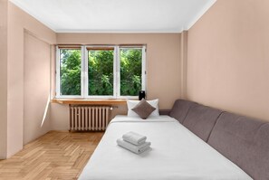 A bedroom with a bed, a window with a view of greenery, a radiator, and a wooden floor. - Sołtyka Comfort Apartment (Kraków)