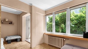 Quarto com uma janela grande, um radiador, um banco e uma porta que dá para outro espaço.