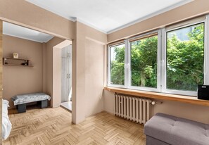 Ein Zimmer mit einem großen Fenster, einem Heizkörper, einer Bank und einer Tür zu einem weiteren Raum.