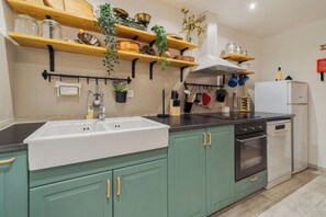Eine Küche mit einem weißen Spülbecken, grünen Schränken, Holzböden und verschiedenen Küchenutensilien.