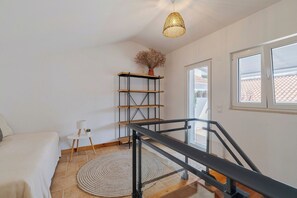 Ein Schlafzimmer mit einem Bett, einem kleinen Tisch mit Lampe, einer Weidenhängelampe, einem Holzbodenregal und einer Treppe.