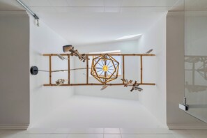 Ein schlichter Raum mit einer geometrischen Leuchte, einem großen Fenster und einer weißen Decke.