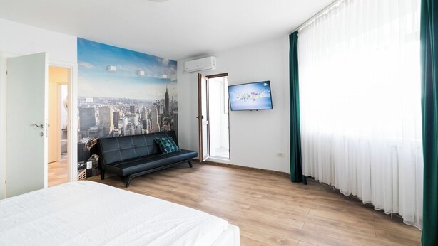 A hotel room with a bed, a sofa, a TV, and a cityscape mural on the wall. - City View Studio: Your Cozy Urban Retreat (Bucharest)