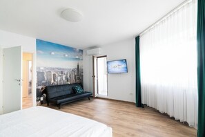 Ett hotellrum med en säng, en soffa, en tv och en väggmålning som föreställer en stadsbild.