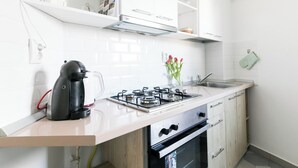 A modern kitchen with white cabinetry, a gas stove, a coffee maker, and a sink. - City View Studio: Your Cozy Urban Retreat (Bucharest)