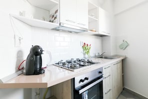 Une cuisine moderne avec des meubles blancs, une cuisinière à gaz, une machine à café et un évier.