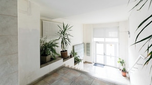 A hallway with tiled flooring, potted plants, a radiator, a door, and a staircase. - City View Studio: Your Cozy Urban Retreat (Bucharest)