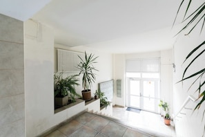 Un couloir avec un sol carrelé, des plantes en pot, un radiateur, une porte et un escalier.