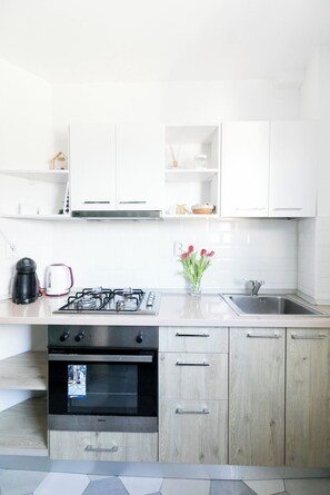 Ett modernt kök med vita skåp, en gasspis, en kaffebryggare och en vas med röda blommor.