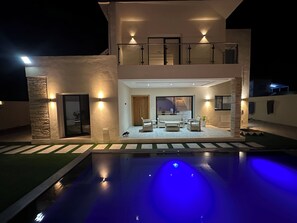 A modern two-story house with a swimming pool, outdoor seating, and a well-lit entrance. - Discover our magnificent Cercina villa, nestled in the heart of the tourist area (Sfax)