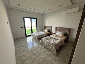 A bedroom with two beds, a sliding glass door to a balcony, and a ceiling with recessed lighting. - Discover our magnificent Cercina villa, nestled in the heart of the tourist area (Sfax)