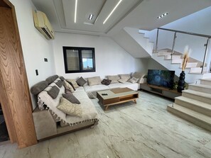 A modern living room with a sectional sofa, a coffee table, a flat-screen TV, and a staircase. - Discover our magnificent Cercina villa, nestled in the heart of the tourist area (Sfax)