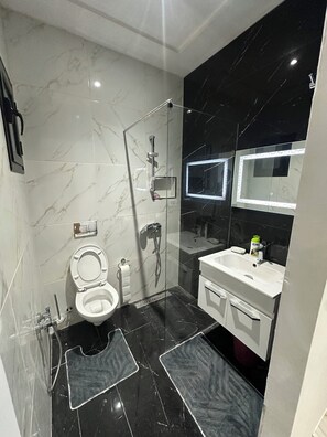 A modern bathroom with a glass-enclosed shower, a toilet, a sink, and a mirror with integrated lighting. - Discover our magnificent Cercina villa, nestled in the heart of the tourist area (Sfax)