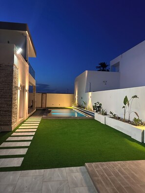 Ein modernes Haus mit Swimmingpool, Rasen aus Kunstgrün und einer Steinmauer.